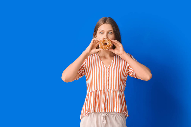 Mujer joven divertida con rosquilla dulce sobre fondo de color - Foto, imagen