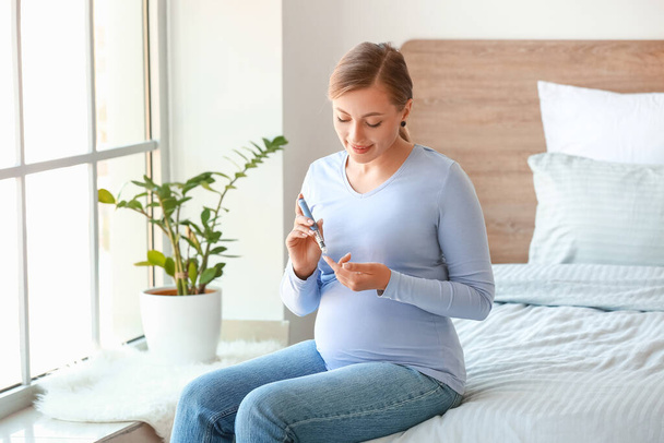 Pregnant diabetic woman measuring blood sugar level at home - Photo, Image