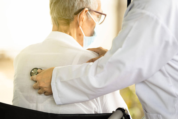 Крупним планом жіночу руку лікаря за допомогою стетоскопа, що слухає серцебиття та дихання пацієнта старшого віку, лікар перевіряє серце та легені літньої жінки ззаду тіла стетоскопом
 - Фото, зображення