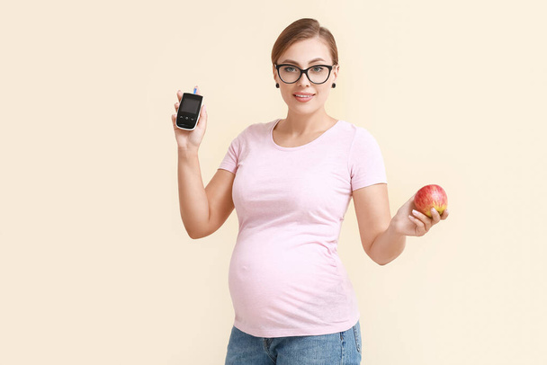Kobieta w ciąży z cukrzycą z cyfrowym glukometrem i jabłkiem na jasnym tle - Zdjęcie, obraz