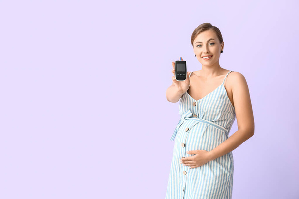 Femme diabétique enceinte avec glucomètre numérique sur fond de couleur - Photo, image