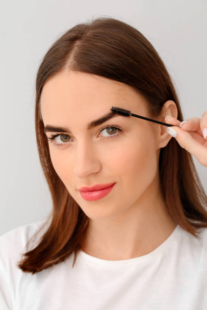 Young woman undergoing eyebrow correction procedure on light background - Photo, Image