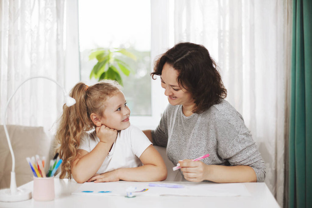 Äiti auttaa tytärtään läksyissä. Äiti opettaa tytön piirtämään. Kotiopetus, verkkokoulutus - Valokuva, kuva