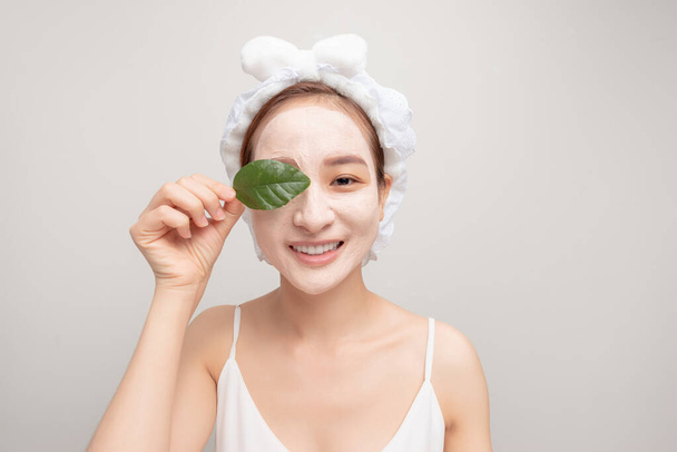 a smiling girl with a white towel on her head applied a clay moisturizing mask - Photo, image