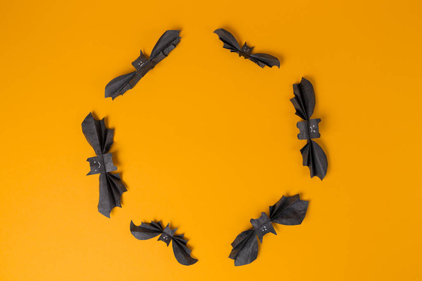 Los murciélagos hechos de papel están dispuestos en un círculo sobre un fondo naranja. Copiar espacio. Acostado. El concepto de Halloween, y decoraciones navideñas. - Foto, Imagen
