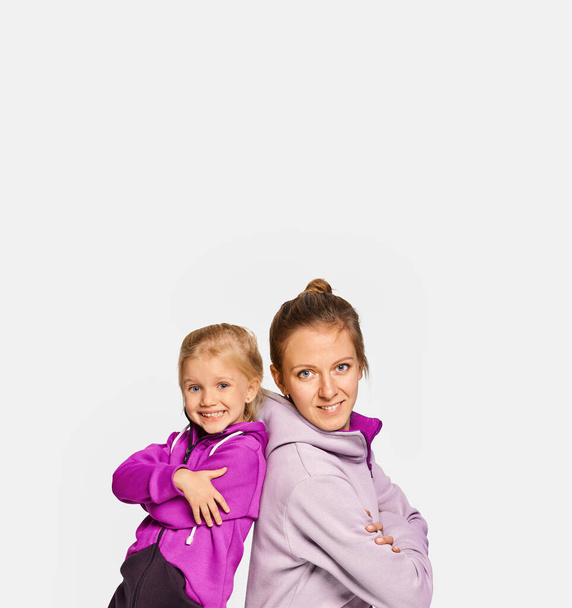 Lächelndes blondes Mädchen und Frau in stylischen Jumpsuits mit Kapuze posieren vor grauem Hintergrund. Nette Tochter 4-5 Jahre alt umarmt ihre Mutter. Attrappe kopieren Raum Lifestyle-Konzept. - Foto, Bild