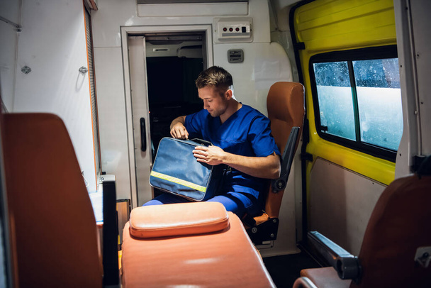 Medical worker on duty, surching for something in his medical kit in an ambulance - Photo, Image