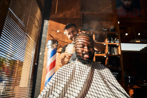 Fröhlicher Friseur, der Talkumpuder auf Kundenhals aufträgt - Foto, Bild