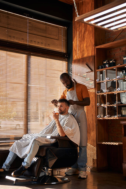 Vousatý holič stříhání klientské vlasy s nůžkami - Fotografie, Obrázek