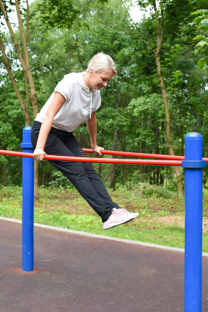 woman in the park is engaged in gymnastics. girl on the horizontal bar - Foto, Imagem