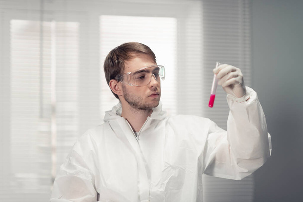 Portrét mladého vědce v ochranných brýlích držícího zkumavku s červenou tekutinou - Fotografie, Obrázek
