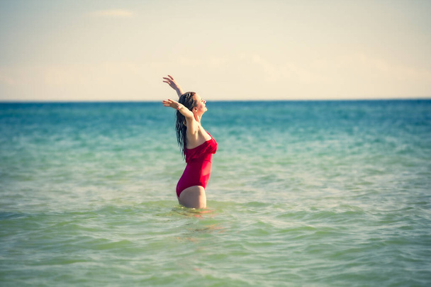 A young slender, beautiful European middle-aged woman is swimming in the sea, a mature brunette in a red bathing suit is enjoying her summer vacation. Freedom and cheerfulness concept - Photo, Image