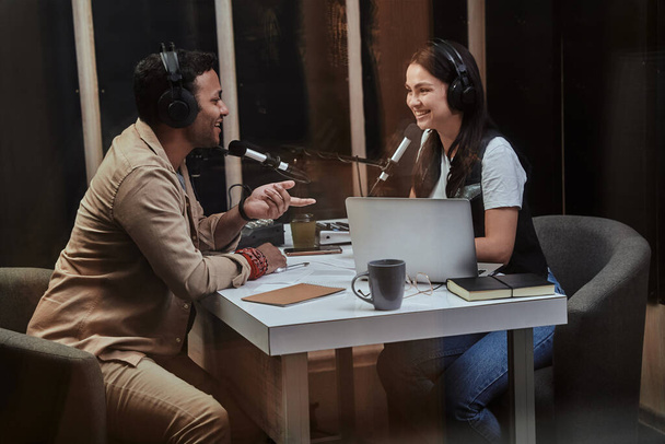Portait két boldog rádió házigazda, fiatal férfi és nő mosolyog, miközben megvitatják a különböző témákat, moderálása élő show stúdióban - Fotó, kép