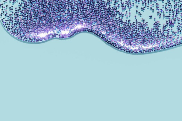 διαφανές υγρό με μωβ glitter ρίχνει πάνω από ένα παστέλ μπλε φόντο - Φωτογραφία, εικόνα