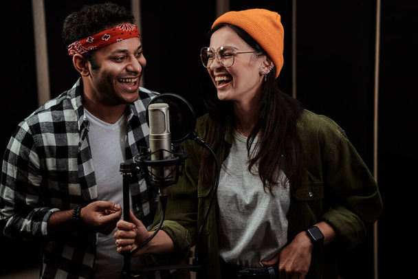 Portré vidám fiatal férfi és nő, duett énekel egy kondenzátor mikrofon, miközben rögzíti a dalt egy profi stúdióban - Fotó, kép