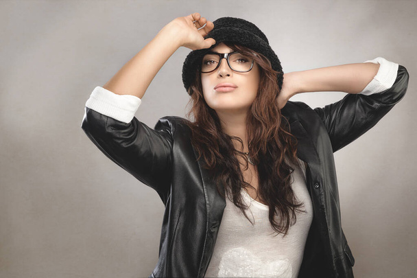 黒の帽子とジャケットを身に着けている黒の秋の流行のファッションでスタイリッシュな若い女性は、現代の眼鏡や腕を白い上に隔離された彼女の帽子に提起ポーズ。眼のケアと眼科 - 写真・画像