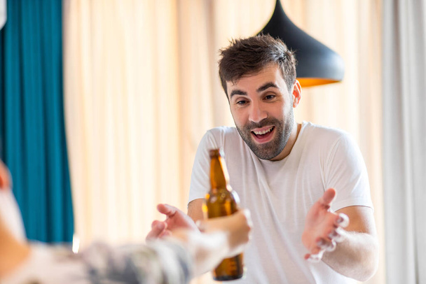 Photo of young bearded man being excited because his friend brought him a bottle of beer. - Valokuva, kuva
