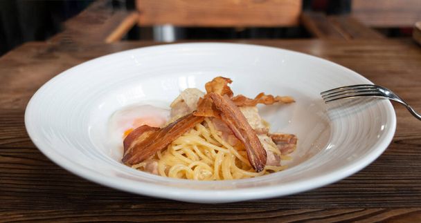 zelfgemaakte spaghetti carbonara met spek en ei op wit bord op houten tafel - Foto, afbeelding