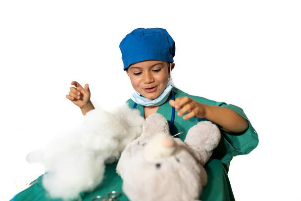 happy child disguised as a surgeon playing doctor operating on a teddy bear - Photo, Image