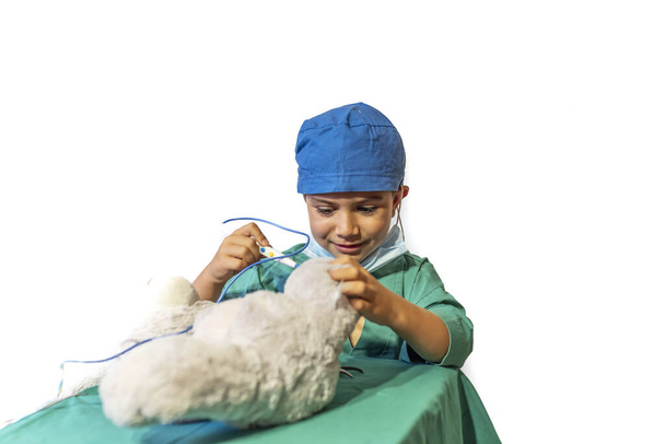 niño feliz disfrazado de cirujano jugando al doctor operando a un oso de peluche - Foto, Imagen