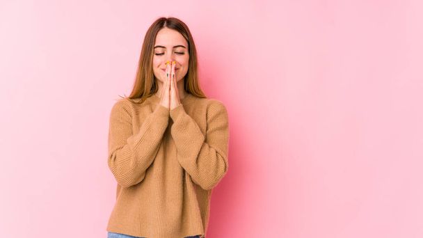 Young caucasian woman isolated on pink background holding hands in pray near mouth, feels confident. - Photo, Image