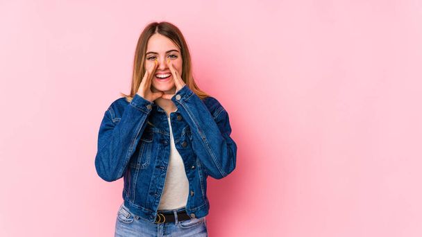 Young caucasian woman isolated on pink background saying a gossip, pointing to side reporting something. - Photo, Image