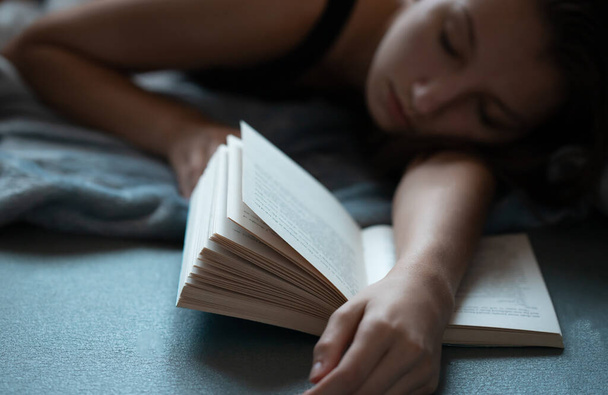 Ένα νεαρό κορίτσι που διαβάζει ένα βιβλίο. Κορίτσι που σπουδάζει για τις εξετάσεις της από ένα βιβλίο. Το κορίτσι αποκοιμήθηκε ενώ μελετούσε.. - Φωτογραφία, εικόνα