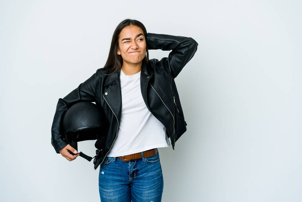 Молода азіатка тримає шолом мотоцикла над ізольованим тлом, торкаючись голови, думаючи і роблячи вибір
. - Фото, зображення