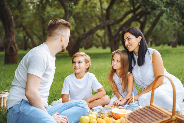 Happy family with two children relaxing on the lawn during a picnic in the green garden. - Photo, Image