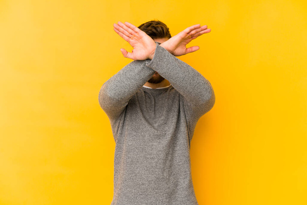 Young caucasian man isolated on yellow background keeping two arms crossed, denial concept. - Photo, Image