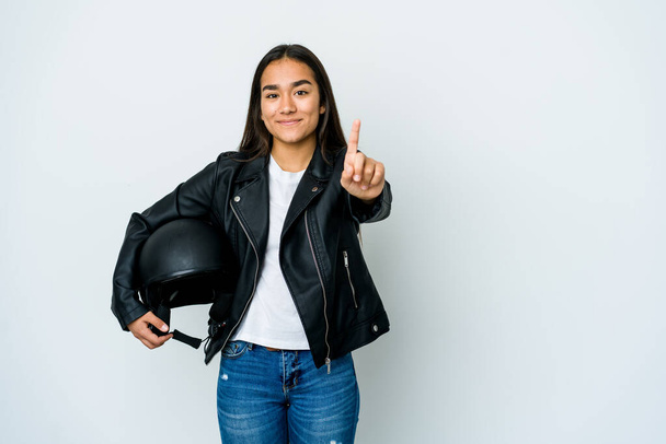 Joven mujer asiática sosteniendo un casco de moto sobre fondo aislado mostrando el número uno con el dedo. - Foto, imagen