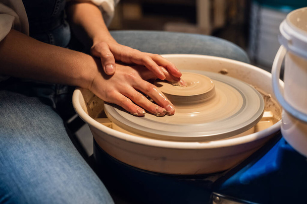 hermosas manos de una joven, manchadas con arcilla al modelar una olla sobre una rueda de alfarero en el taller. - Foto, imagen