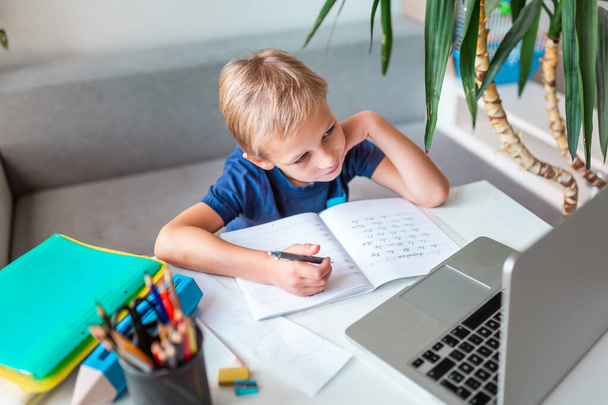 Little young school boy working at home with a laptop and class notes studying in a virtual class. Distance education and learning, e-learning, online learning concept during quarantine - Фото, зображення