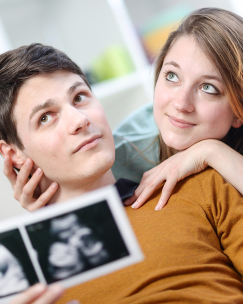 Beautiful couple imagines the future of their unborn child with ultrasound pictures in hands - Photo, Image