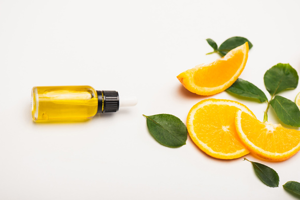 bottle of fresh homemade citrus essence near juicy orange slices and rose leaves on white - Valokuva, kuva
