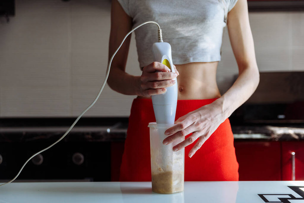 El blendırlı kadın muzlu, tatlı protein milkshake yapıyor. Spor salonundan sonra beslenme diyeti. Sağlıklı yaşam tarzı - Fotoğraf, Görsel