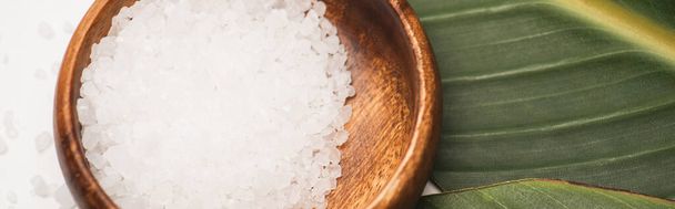 close up view of natural sea salt in wooden bowl on green leaf, banner - Фото, зображення