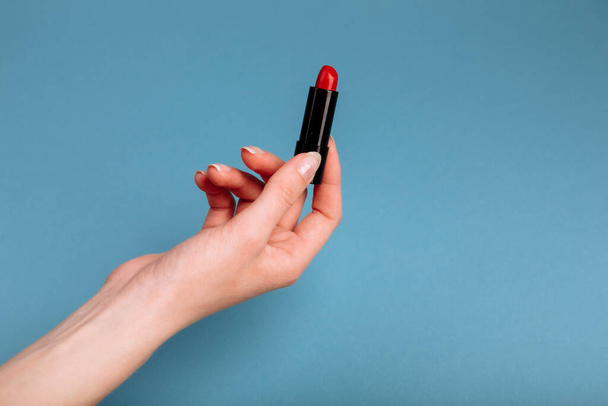 Naiskäsi ottaa punaista huulipunaa. eristetty sinisellä pohjalla - Valokuva, kuva