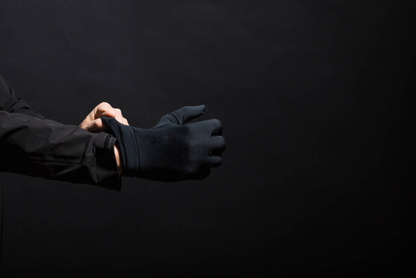 Hand in Hand mit schwarzen Handschuhen eines Verbrechens auf schwarzem Hintergrund. An der Hand werden Handschuhe getragen. Der Mann zieht sich einen schwarzen Handschuh über die Hand. - Foto, Bild