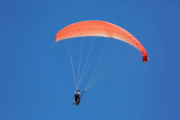 Blauer Gleitschirm-Tandemlehrer mit einem Touristen, der an einem sonnigen Tag mit Wolken in den Himmel fliegt - Foto, Bild