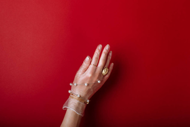 Fashion art hand vrouw in de handschoen bescherming tegen COVID-19 met sieraden geïsoleerd op rode achtergrond. - Foto, afbeelding