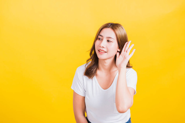 Portrait Asian Thai beautiful young woman listening something with her palm hand behind the ear, studio shot isolated on yellow background, There was copy space, Gossip concept - Foto, Bild