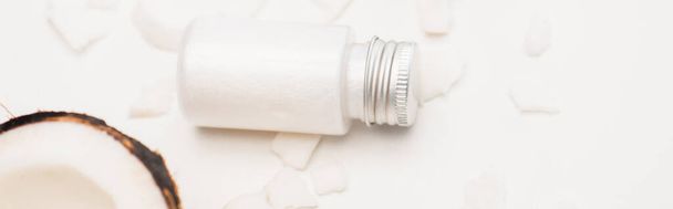bottle of nourishing homemade lotion near coconut half and flakes on white, banner - Photo, Image