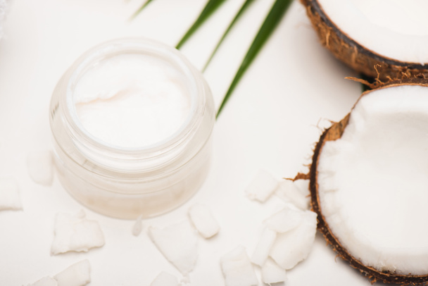 container with homemade cream near palm leaves, coconut halves and flakes on white - Фото, зображення