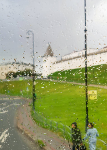 Vue sur le mur du Kremlin Kazan et la rue de la ville par temps pluvieux à travers le verre inondé d'eau. Concentration douce. - Photo, image