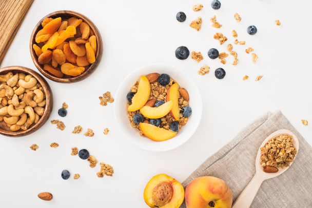 сверху вид вкусной мюсли с орехами, персиком, черникой и сушеными абрикосами, изолированными на белом - Фото, изображение