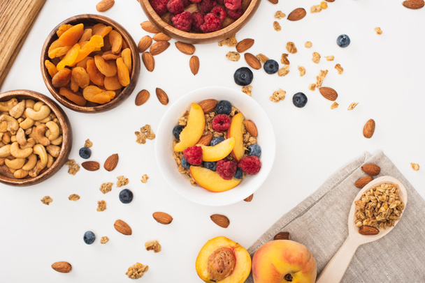 Blick von oben auf köstliches Müsli mit Nüssen, Himbeeren, Pfirsichen, Blaubeeren und getrockneten Aprikosen isoliert auf weiß - Foto, Bild