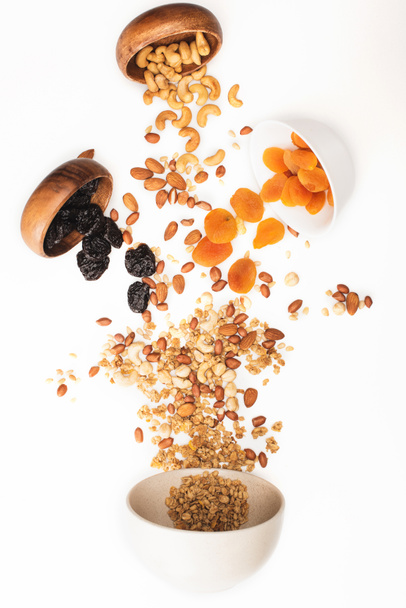 bovenaanzicht van heerlijke granola met noten en gedroogde vruchten verspreid uit kommen geïsoleerd op wit - Foto, afbeelding