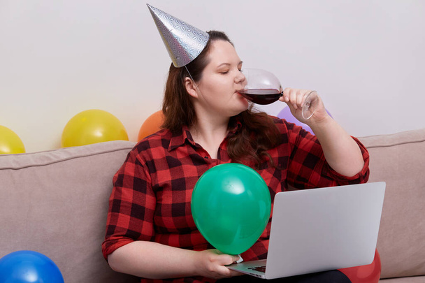 A woman celebrates her birthday during the pandemic and drinks red wine. - Photo, image