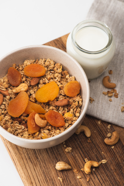 top view of delicious granola with nuts, dried apricots and yogurt on wooden board on white background - Photo, Image